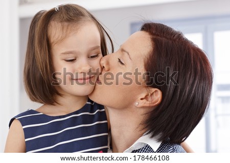 Mother kissing happy little daughter's face.