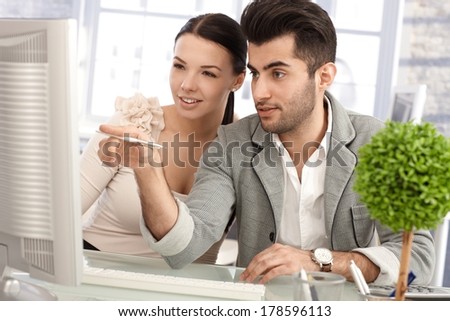 Attractive young businesspeople working together at desk, using computer.