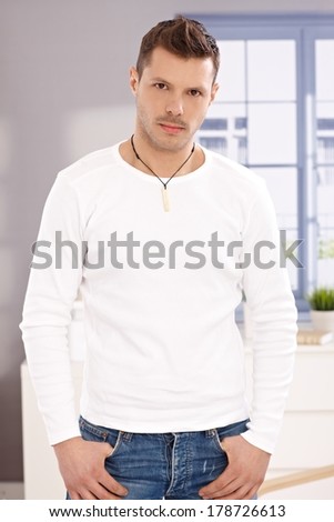 Portrait of serious looking handsome young man standing front of window.