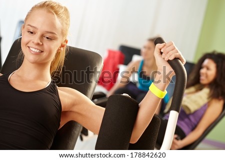 Happy girl doing keep-fit exercises at the gym on weight machine.