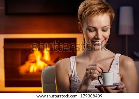 Happy woman sitting by fireplace, drinking coffee, enjoying peace.