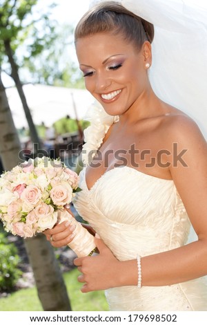Outdoor portrait of beautiful bride with bouquet in wedding gown.