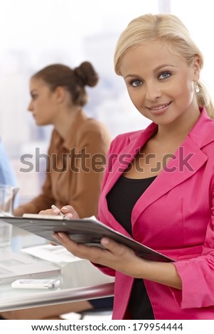 Businesswoman writing notes at businessmeeting, smiling.