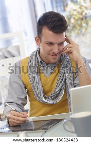 Young man sitting at table working with drawing pad, smiling.