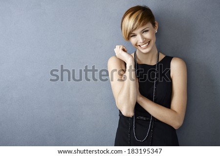 Portrait of happy young woman in black dress and pearls on grey background