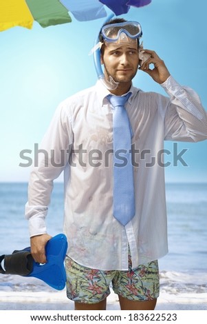 Young businessman using seashell as mobilephone on the beach wearing shirt and tie and scuba diving equipments.