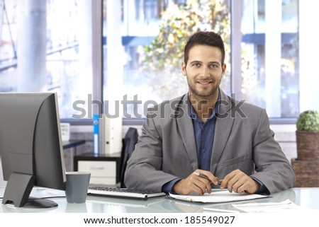 Portrait of happy handsome businessman sitting in bright office at desk, working.