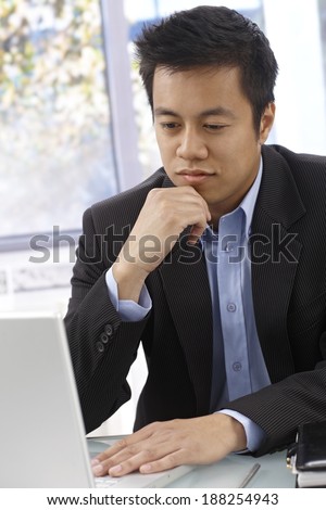 Young Asian businessman working with computer, sitting at desk, thinking.