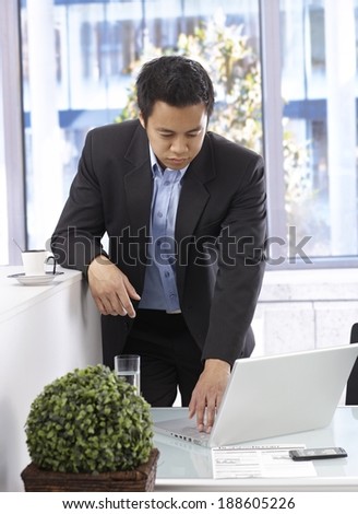 Businessman working with laptop computer, standing at desk.