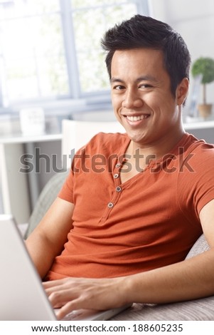 Portrait of happy young man using laptop at home, sitting on sofa, smiling.