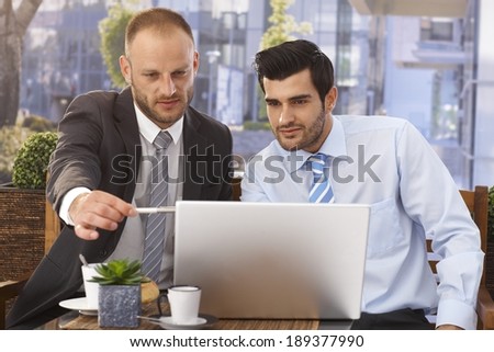 Close up of caucasian businessmen working on laptop at outdoor cafe, pointing at screen with pen, suit and tie.