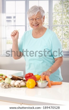Elderly lady preparing healthy food in kitchen, using vegetables and brown bread.
