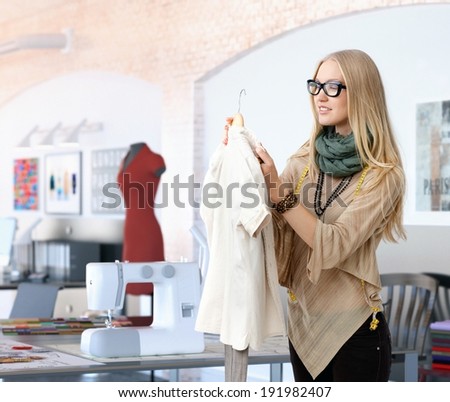 Young trendy blonde caucasian fashion designer woman working at studio. Happy, table with sewing machine.