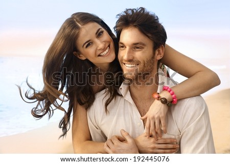 Portrait of happy casual caucasian married couple at the beach. Handsome man, attractive young woman, smiling, looking at camera, embracing.