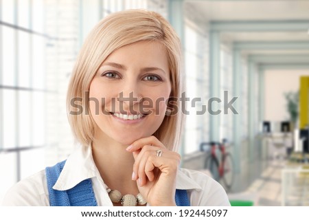 Portrait of happy blond female office worker smiling at workplace.
