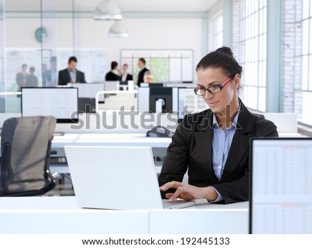 Trustworthy businesswoman working at office desk, using laptop computer.