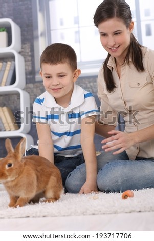 Mum and son having fun with pet rabbit at home, playing on living room carpet.