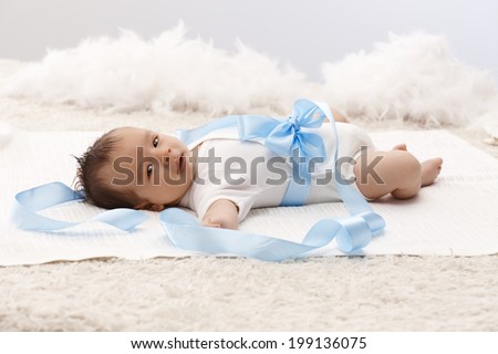 Beautiful baby lying on back in white bodysuit and blue ribbon around waist.