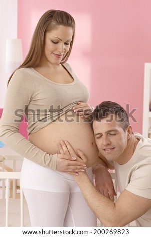 Happy pregnant mother and father listening to heartbeat of baby in tummy.