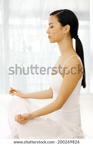 Side view of young woman practicing yoga indoors, relaxing eyes closed.