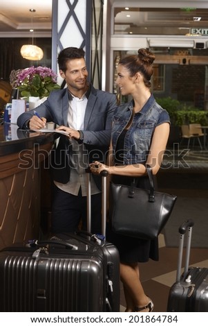 Young couple filling in check in form at hotel reception upon arrival, smiling happy.