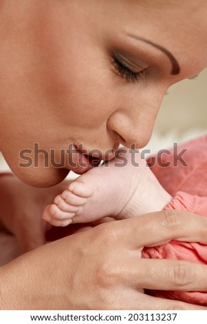 Closeup photo of young mother kissing tiny baby\'s foot eyes closed.