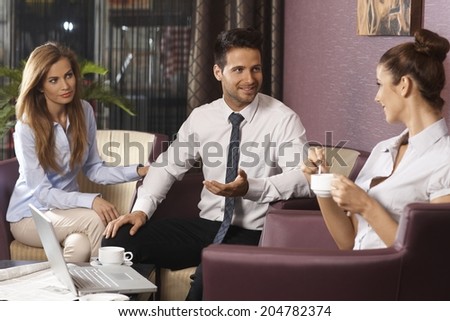 Team of young businesspeople working late, using laptop computer at hotel lobby or bar, having discussion and coffee.