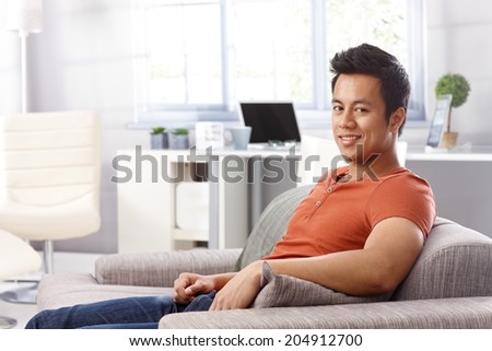 Portrait of handsome young man sitting at home on sofa, smiling, looking at camera.