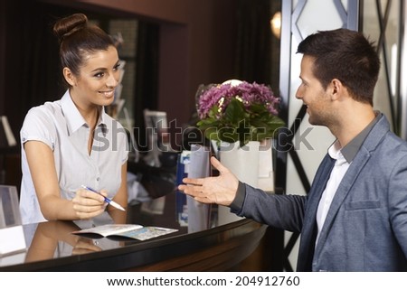 Happy receptionist and guest talking at hotel reception.