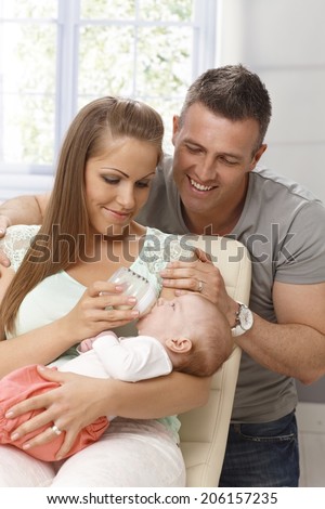 Happy young couple feeding and adoring newborn baby girl, smiling.