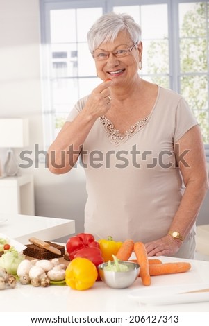 Happy grandmother standing in kitchen using fresh raw materials to prepare healthy food.