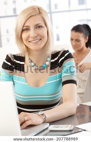 Portrait of caucasian casual blonde businesswoman working with laptop computer in office, smiling.
