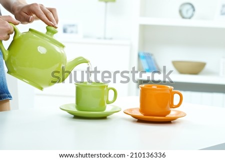 Pouring water from tea kettle to mug high key bright background, table, pastel colors, close up, indoors home.