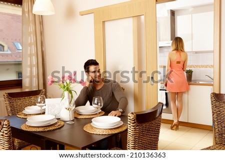 Young couple waiting for dinner guests at home, woman in kitchen cooking.
