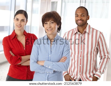 Team of happy caucasian business people standing in office looking at camera smiling, standing, arms crossed.