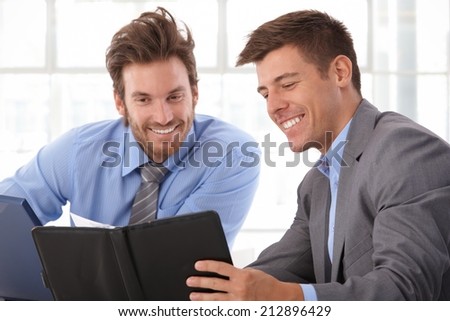 Happy, handsome caucasian businessman looking at personal organizer at business office. Smiling, wearing suit.