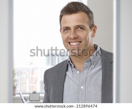Portrait of happy smiling businessman at office. Suit with no tie, looking at camera.