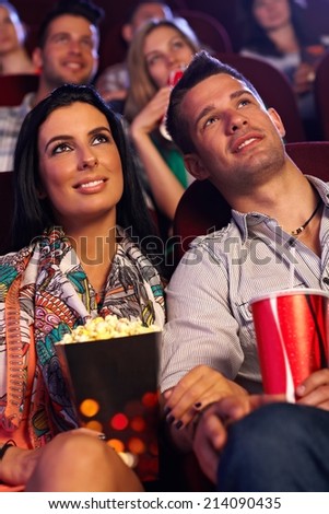 Young couple sitting in movie theater, watching film, having popcorn.