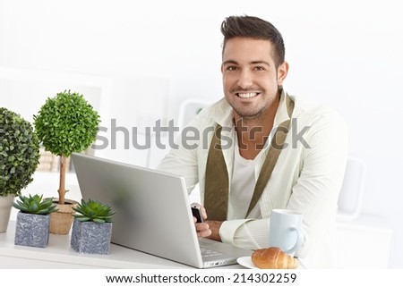 Happy young businessman using laptop and mobile during breakfast.