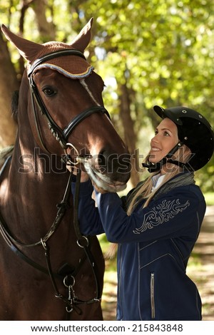 Young female rider looking at horse with love, outdoor photo.