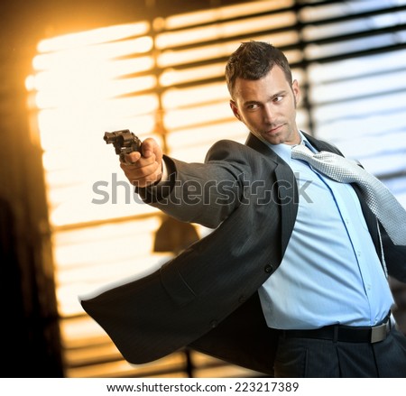 Determined caucasian action hero wearing suit and tie holding gun in hand. Standing, moving, aiming with revolver, inspector, cop, police, policeman, indoor, thriller, crime.