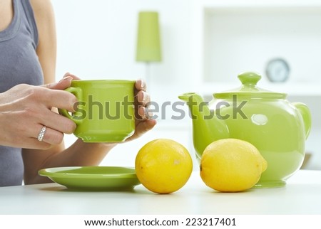 High key still life with tea kettle mug and lemon, pastel colors. Close up hand with ring, holding cup, copyspace.