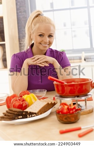 Attractive young female preparing cheese fondue at home, smiling, looking at camera.