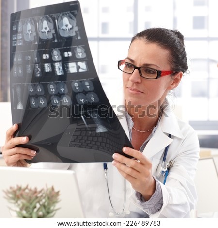 Portrait of female brunette doctor with x-ray image in hand, wearing glasses, stethoscope and lab coat,
