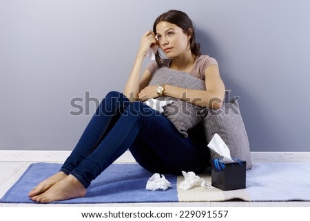 Heart-broken young woman sitting on floor at home, crying, wiping away tears by hanky.