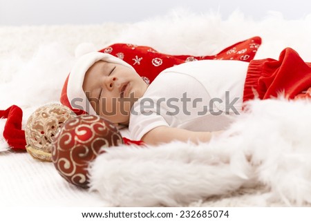 Little baby boy sleeping in santa hat with christmas decoration around him.