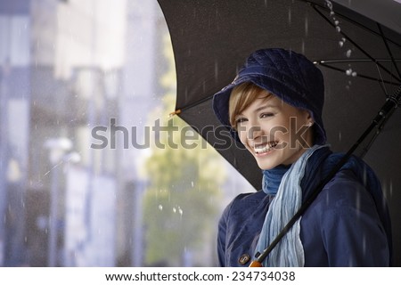 Happy young woman holding umbrella in rain, smiling.