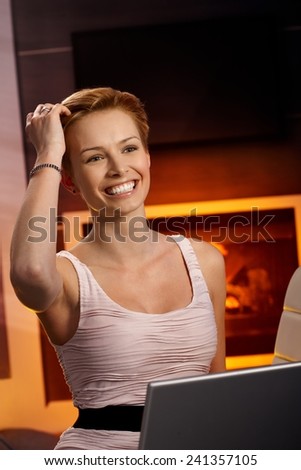 Pretty woman browsing internet at home by fireplace, smiling happy, hand in hair.