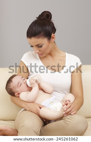 Naked baby fell asleep in mother\'s arms while drinking from feeding bottle.