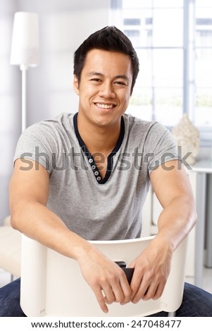 Portrait of happy young casual man sitting on chair, smiling, looking at camera.